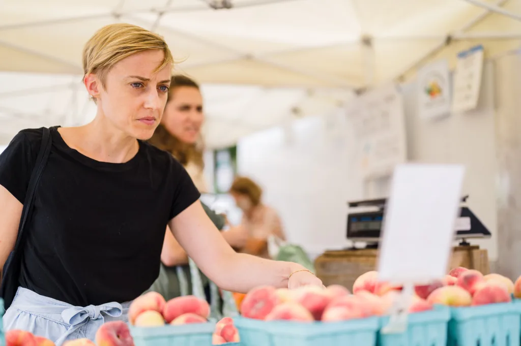 Woman shopping for fresh peaches at Bow Market in Somerville, MA