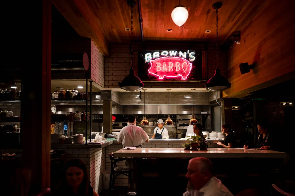 Neon sign for Brown's Bar-B-Q hanging over cooks in the kitchen