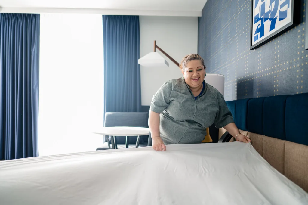 Woman making the bed with a smile at Cambria's hotel in Somerville, MA