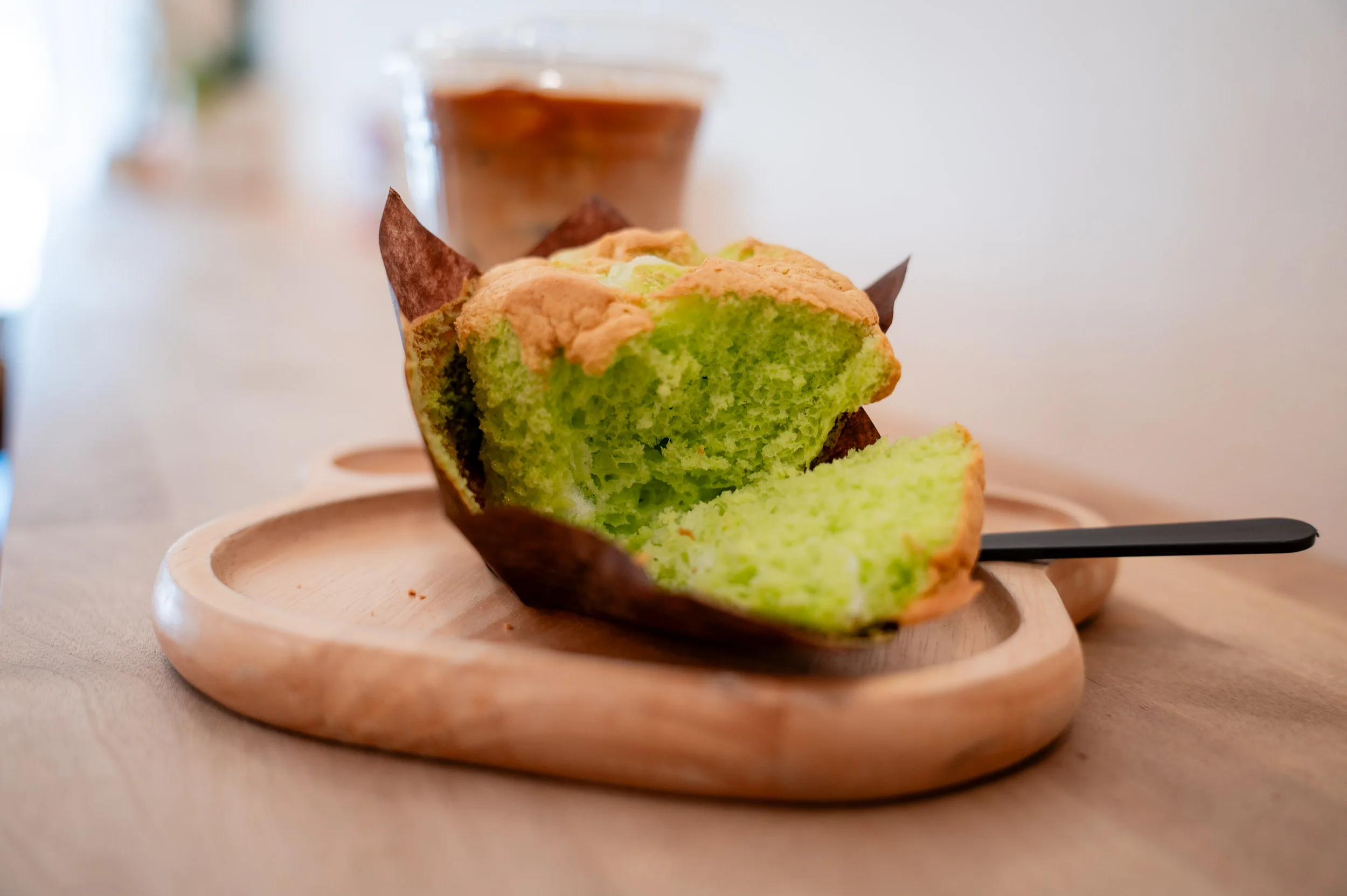 pandan cake slice on a wooden board with an iced drink in the background